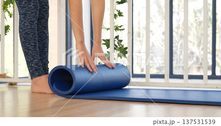 Woman hands rolled up yoga mat on gym floor in yoga fitness training room. Home workout woman close up hands rolling foam yoga gym mat. Woman barefoot home workout sportive healthy lifestyle concept 137531539