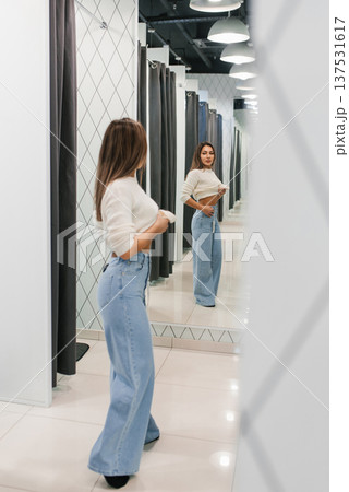 Young Woman Adjusting Jeans In Store Mirror Young Woman Adjusting Jeans In Store Mirror 137531617