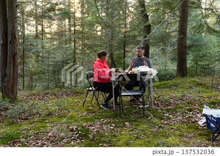 A couple delights in a warm and intimate outdoor dining experience, nestled within a tranquil forest setting that radiates beauty during the enchanting golden hour 137532036