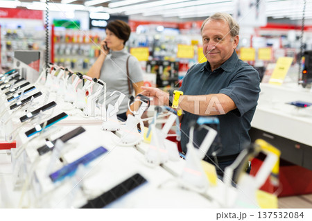 Elderly male customer looking for a deal on smart watches in big electronics store Elderly male customer looking for a deal on smart watches in big electronics store 137532084