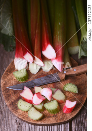 Fresh rhubarb stems and cut pieces on round chopping board 137532128