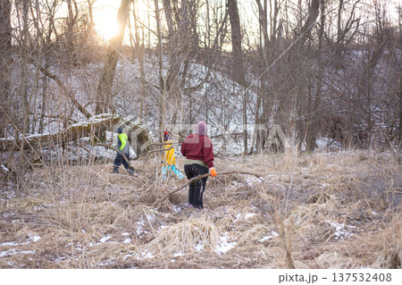 Community members engage in outdoor restoration efforts in a winter landscape, clearing brush and fostering growth as the sun rises in a serene woodland area 137532408