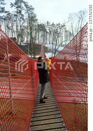 Father holding toddler on red suspension bridge in winter forest Father holding toddler on red suspension bridge in winter forest 137532592