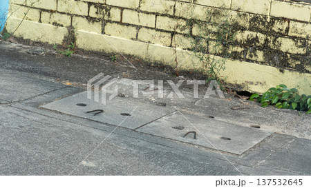 High angle view of concrete drainage manhole covers on a city street in Thailand. Urban infrastructure and sewage system along a weathered yellow brick wall in a residential area. 137532645