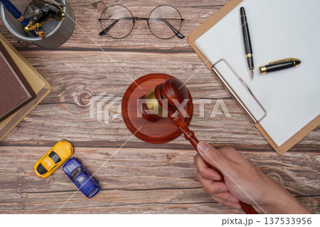 Hand holding gavel with cars and legal documents on table Hand holding gavel with cars and legal documents on table 137533956