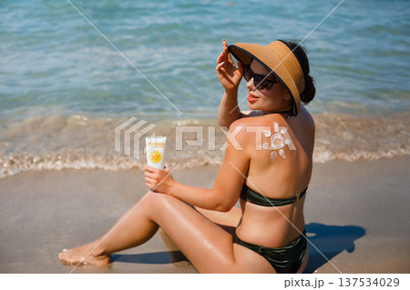 Woman enjoying summer beach vacation holding sunscreen lotion with suncream sun symbol on her back Woman enjoying summer beach vacation holding sunscreen lotion with suncream sun symbol on her back 137534029