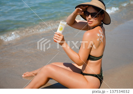 Woman Applying Sun Cream on Tanned Shoulder In Form Of The Sun. Sun Protection.Sun Cream. Skin and Body Care. Girl Using Sunscreen to Skin. Female Holding Suntan Lotion. Woman Applying Sun Cream on Tanned Shoulder In Form Of The Sun. Sun Protection.Sun Cream. Skin and Body Care. Girl Using Sunscreen to Skin. Female Holding Suntan Lotion. 137534032