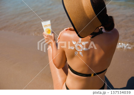 Woman enjoying sunny beach lifestyle holding sunscreen lotion with decorative suncream sun symbol Woman enjoying sunny beach lifestyle holding sunscreen lotion with decorative suncream sun symbol 137534039
