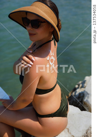 Beautiful woman relaxing on Mediterranean beach holding sunscreen lotion Beautiful woman relaxing on Mediterranean beach holding sunscreen lotion 137534058