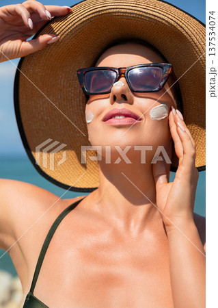 Beautiful woman enjoying sun protection skincare routine applying sunscreen cream on face and moisturizing skin with suncream lotion during beach holiday Beautiful woman enjoying sun protection skincare routine applying sunscreen cream on face and moisturizing skin with suncream lotion during beach holiday 137534074