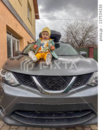 Toddler Sitting on Hood of Gray Suv in Driveway Toddler Sitting on Hood of Gray Suv in Driveway 137534330