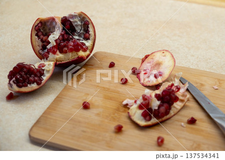 Cut pomegranate on cutting board with scattered arils Cut pomegranate on cutting board with scattered arils 137534341