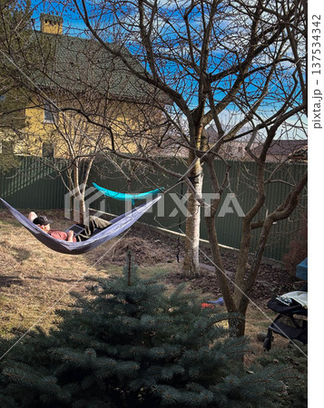 Person relaxing in hammock in backyard with stroller Person relaxing in hammock in backyard with stroller 137534342