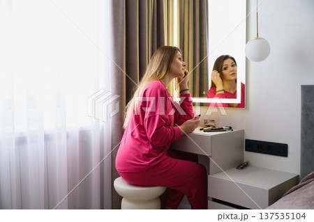 Young woman applying mascara at mirror vanity table Young woman applying mascara at mirror vanity table 137535104