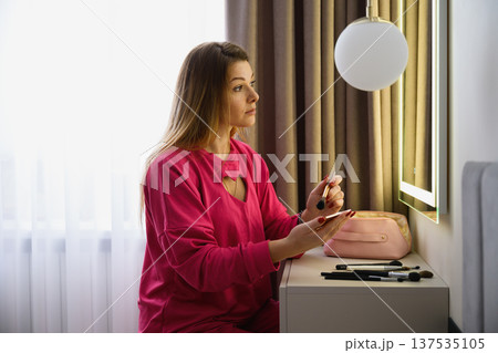 Young woman applying makeup at vanity mirror 137535105