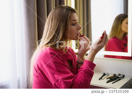 Young woman applying lipstick at vanity mirror Young woman applying lipstick at vanity mirror 137535109