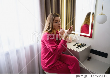 Young woman applying lipstick at vanity mirror Young woman applying lipstick at vanity mirror 137535110