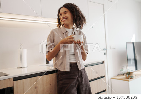 Female Expressing Happiness While Holding Mug In Comfortable Kitchen Environment With Bright Sunlight 137536239