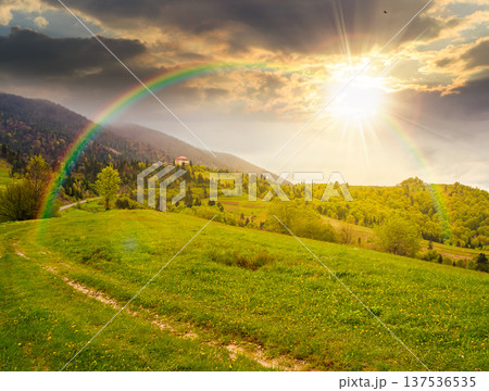 remote countryside in mountain landscape at sunset. hazy weather during spring in evening light. dirt road through lush green pasture on a hill. alpine vista with deciduous trees under rainbow remote countryside in mountain landscape at sunset. hazy weather during spring in evening light. dirt road through lush green pasture on a hill. alpine vista with deciduous trees under rainbow 137536535