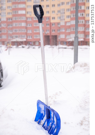 Blue snow shovel in urban winter scene with snowy background Blue snow shovel in urban winter scene with snowy background 137537513