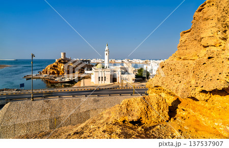 A scenic view of the mosque and Al Ayjah watchtowers along the waterfront in Sur, Oman, showcasing traditional architecture and a docked dhow boat. 137537907