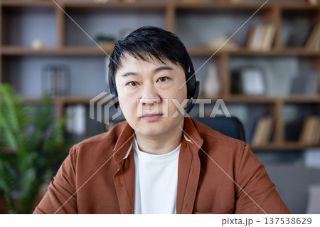 Man in headset looking directly at camera, having a video conference call from home office, representing remote work, technical support, or online communication Man in headset looking directly at camera, having a video conference call from home office, representing remote work, technical support, or online communication 137538629