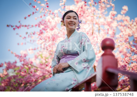 woman in yukata (kimono dress) with sakura flower or cherry blossom blooming in garden 137538748