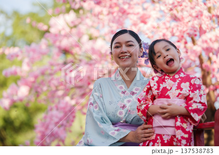 woman and child girl in yukata (kimono dress) on red bridge with sakura flower or cherry blossom blooming in garden 137538783