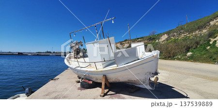 A small fishing boat sits on a concrete dock beside calm blue water. A small fishing boat sits on a concrete dock beside calm blue water. 137539889