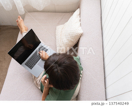 Elderly woman working on laptop in cozy home setting with relaxed comfort 137540249