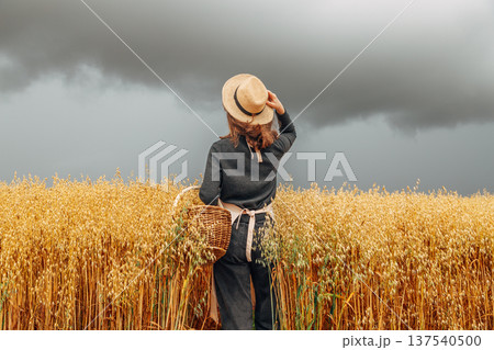 Girl in a wheat field wearing a straw hat on a cloudy day. Back view Girl in a wheat field wearing a straw hat on a cloudy day. Back view 137540500