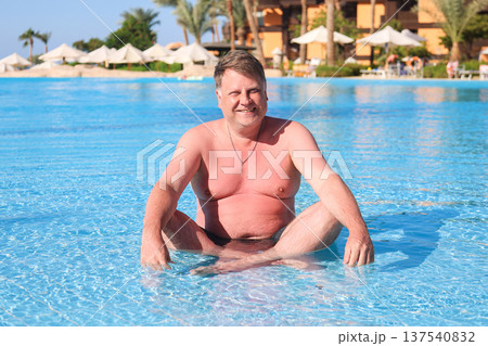 Happy overweight man sitting in the water of a shallow pool 137540832
