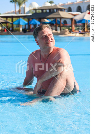Happy overweight man sitting in the water of a shallow pool 137540833