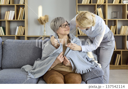 Senior woman wrapped in blanket with caregiver offering supportive home care Senior woman wrapped in blanket with caregiver offering supportive home care 137542114
