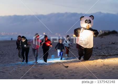 Kids running with lights and panda costume on beach at night Kids running with lights and panda costume on beach at night 137542148