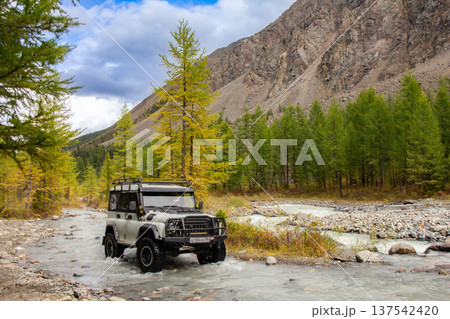 UAZ Hunter tourist SUV conquers a harsh mountain river Aktru flowing from glacier. Alpine camps and valley. Autumn sunny day. Landscape Mountains in Siberia. Chuiskiy Range, Altai Republic, Russia 137542420