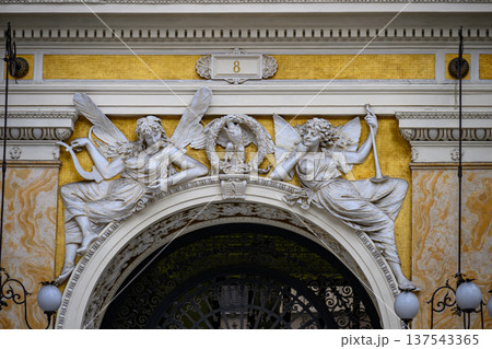 Ornate sculptural detail in Galleria Umberto I, Naples, Italy. Two classical figures, likely representing allegorical themes, flank an eagle over an archway. The figures are depicted in flowing robes Ornate sculptural detail in Galleria Umberto I, Naples, Italy. Two classical figures, likely representing allegorical themes, flank an eagle over an archway. The figures are depicted in flowing robes 137543365