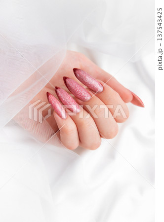 Woman's hand displaying pink shimmering stiletto nails Woman's hand displaying pink shimmering stiletto nails 137543425