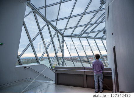 Lyon, france. December 28, 2023. Person standing inside musee des confluences in lyon, looking out at the city and river through the geometric glass roof Lyon, france. December 28, 2023. Person standing inside musee des confluences in lyon, looking out at the city and river through the geometric glass roof 137543459