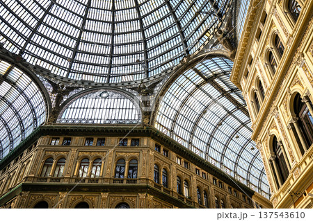 Galleria Umberto I in Naples, Italy, features an ornate glass dome ceiling supported by intricate wrought iron framework. The architectural design is rich with classical details. 137543610