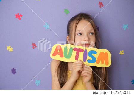 A pensive sweet beautiful girl looks away with a thoughtful look holding a colorful inscription autism on a cardboard 137545011