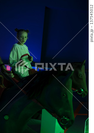 A child rides a game horse in an amusement park. 137545012