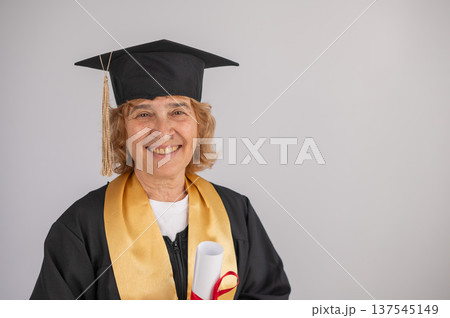 Happy senior woman in graduation gown holding diploma on white background. Happy senior woman in graduation gown holding diploma on white background. 137545149