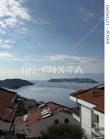 Coastal view with red roof houses, calm sea, and distant islands under a blue sky background 137545843