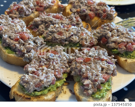 Tuna salad crostini with avocado spread and diced tomatoes on a white plate perfect for parties 137545850