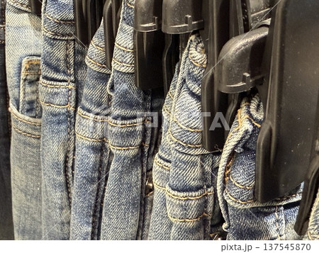 Row of blue denim jeans hanging on black plastic hangers in a retail clothing store Row of blue denim jeans hanging on black plastic hangers in a retail clothing store 137545870