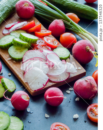 Red cherry tomatoes, radish, herbs and cucumbers sprinkled with sea salt on wooden board on table. Red cherry tomatoes, radish, herbs and cucumbers sprinkled with sea salt on wooden board on table. 137546320