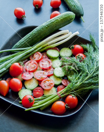 Fresh red cherry tomatoes, green leek and cucumber in pan on black background, top view. 137546350