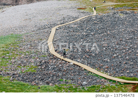 Russia, Teriberka, People walk along a wooden path at sunset, the coast of the Barents Sea, the rocky shore with colourful arctic carpet of moss, yagel, Tundra at autumn, Murmansk 137546478