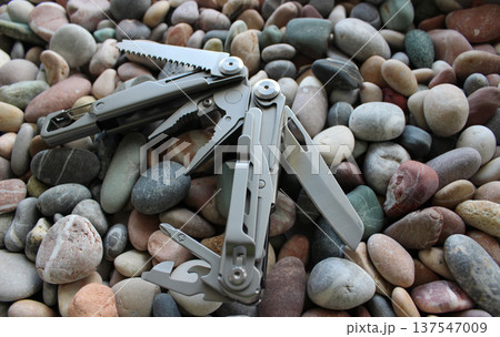 Half-opened full metal multi-tool with different blades and folding screwdrivers on colored pebbles 137547009